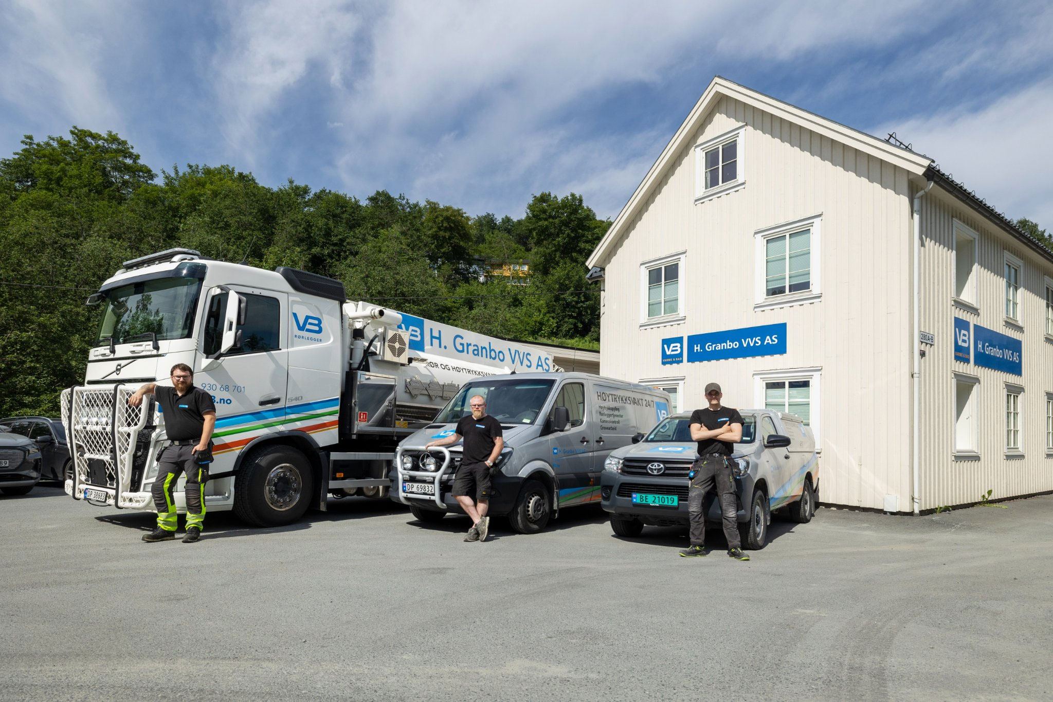 Tre rørleggere ved hver sin arbeidsbil og en spylebil utenfor lokalene til H. Granbo VVS i solskinnsvær.
